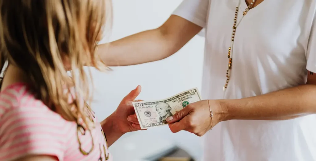 子どもにお金を手渡す親の画像